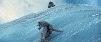 Movie still from “Against the Ice” (2022), directed by Peter Flinth – A man riding a sled down the side of a snow covered slope; Wide shot, Overhead angle