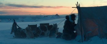 Movie still from “Against the Ice” (2022), directed by Peter Flinth – A group of dogs pulling a sled down a snow covered slope; Extreme Wide shot, High angle