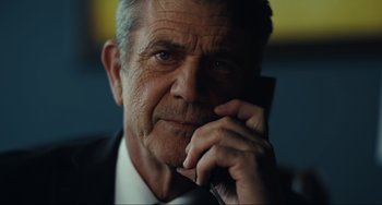 An older man in a suit is talking on a cell phone