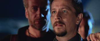 Movie still from “Air Force One” (1997), directed by Wolfgang Petersen – A man's face with a blurry image of a man in the background; Close Up shot, Low angle