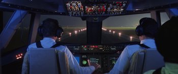 Movie still from “Air Force One” (1997), directed by Wolfgang Petersen – A man flying an airplane at night in the cockpit; Wide shot, Low angle