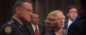 Movie still from “Air Force One” (1997), directed by Wolfgang Petersen – A man and a woman standing next to each other in front of another man; Close Up shot, Over the shoulder angle