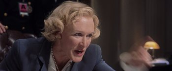 Movie still from “Air Force One” (1997), directed by Wolfgang Petersen – An older woman with blonde curly hair wearing a blue suit; Close Up shot, Over the shoulder angle