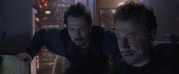 Movie still from “Air Force One” (1997), directed by Wolfgang Petersen – A man standing next to another man in a dark room; Close Up shot, Low angle