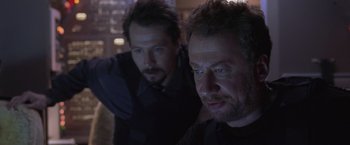 Movie still from “Air Force One” (1997), directed by Wolfgang Petersen – Two men are looking at the camera in a dark room; Close Up shot, Over the shoulder angle