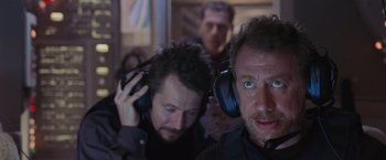 Movie still from “Air Force One” (1997), directed by Wolfgang Petersen – A man with headphones is standing next to another man; Close Up shot, Over the shoulder angle