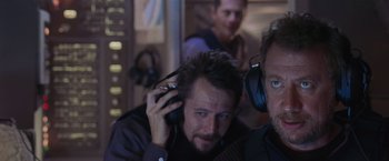 Movie still from “Air Force One” (1997), directed by Wolfgang Petersen – A man with a beard is listening to headphones; Close Up shot, Over the shoulder angle