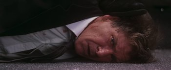 Movie still from “Air Force One” (1997), directed by Wolfgang Petersen – A person laying on the ground wearing a suit; Close Up shot, Overhead angle