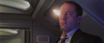 Movie still from “Air Force One” (1997), directed by Wolfgang Petersen – A man in a suit and tie with a light shining on his head; Close Up shot, Low angle