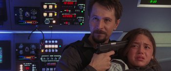 Movie still from “Air Force One” (1997), directed by Wolfgang Petersen – A man holding a gun while standing next to a control panel; Close Up shot, Over the shoulder angle