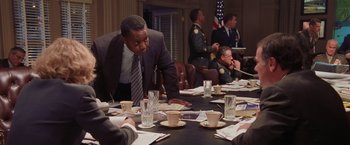 Movie still from “Air Force One” (1997), directed by Wolfgang Petersen – A group of people sitting at a table with cups of coffee; Medium shot, Over the shoulder angle