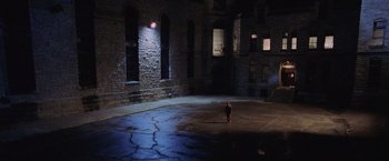 Movie still from “Air Force One” (1997), directed by Wolfgang Petersen – A person standing in a dark room in front of a brick wall; Extreme Wide shot, High angle
