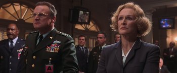 Movie still from “Air Force One” (1997), directed by Wolfgang Petersen – A group of people standing in front of a television; Medium shot, Low angle