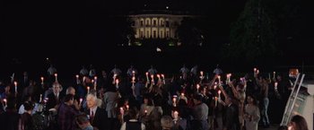 Movie still from “Air Force One” (1997), directed by Wolfgang Petersen – A group of people holding lit candles in front of a white house; Extreme Wide shot, High angle