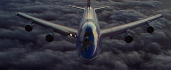 Movie still from “Air Force One” (1997), directed by Wolfgang Petersen – An airplane flying through the sky with a person in the back; Extreme Wide shot, Overhead angle