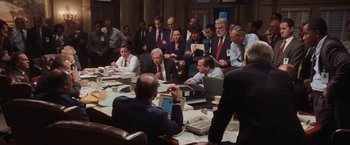 Movie still from “Air Force One” (1997), directed by Wolfgang Petersen – A group of people sitting around a table with papers; Wide shot, High angle