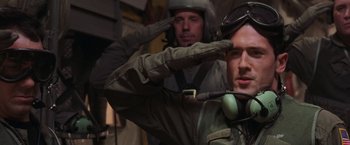 Movie still from “Air Force One” (1997), directed by Wolfgang Petersen – Two men in flight suits are saluting in a hangar; Close Up shot, Low angle