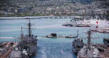 Movie still from “Aircraft Carrier: Guardian of the Seas” (2016), directed by Stephen Low – Several ships are docked in the water near a city; Extreme Wide shot, High angle