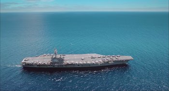 Movie still from “Aircraft Carrier: Guardian of the Seas” (2016), directed by Stephen Low – An aerial view of an aircraft carrier in the ocean; Extreme Wide shot, High angle