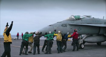 Movie still from “Aircraft Carrier: Guardian of the Seas” (2016), directed by Stephen Low – A group of people standing around a fighter jet; Wide shot, High angle