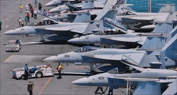 Movie still from “Aircraft Carrier: Guardian of the Seas” (2016), directed by Stephen Low – A group of fighter jets sitting on top of an airport runway; Extreme Wide shot, High angle