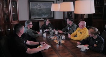 Movie still from “Aircraft Carrier: Guardian of the Seas” (2016), directed by Stephen Low – A group of people sitting around a wooden table; Medium shot, Over the shoulder angle