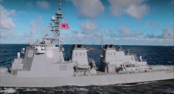 Movie still from “Aircraft Carrier: Guardian of the Seas” (2016), directed by Stephen Low – A large ship in the water with a flag on it; Extreme Wide shot, High angle