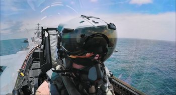 Movie still from “Aircraft Carrier: Guardian of the Seas” (2016), directed by Stephen Low – A person wearing a helmet on top of a boat; Close Up shot, Over the shoulder angle