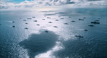 Movie still from “Aircraft Carrier: Guardian of the Seas” (2016), directed by Stephen Low – Many boats in the water in the ocean; Extreme Wide shot, High angle