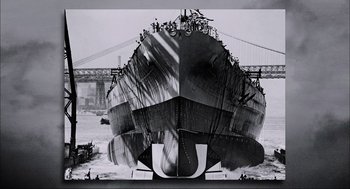 Movie still from “Aircraft Carrier: Guardian of the Seas” (2016), directed by Stephen Low – A black and white photo of a large boat in the water; Extreme Wide shot, Low angle