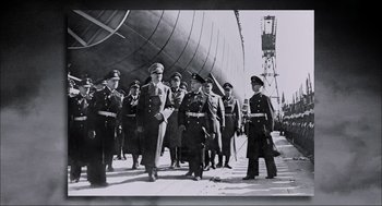 Movie still from “Aircraft Carrier: Guardian of the Seas” (2016), directed by Stephen Low – A black and white photo of a group of men in military uniforms; Wide shot, Low angle