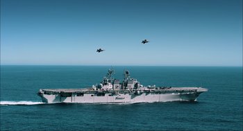 Movie still from “Aircraft Carrier: Guardian of the Seas” (2016), directed by Stephen Low – Two fighter jets flying over a large ship in the ocean; Extreme Wide shot, Low angle