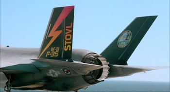 Movie still from “Aircraft Carrier: Guardian of the Seas” (2016), directed by Stephen Low – View of the tail of a jet fighter plane; Wide shot, Low angle