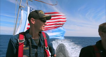 Movie still from “Aircraft Carrier: Guardian of the Seas” (2016), directed by Stephen Low – A man wearing a hat and a uniform on a boat in the ocean; Medium shot, Low angle