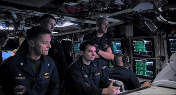 Movie still from “Aircraft Carrier: Guardian of the Seas” (2016), directed by Stephen Low – A group of men sitting on a boat in the water; Medium shot, Over the shoulder angle