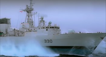 Movie still from “Aircraft Carrier: Guardian of the Seas” (2016), directed by Stephen Low – A large white boat in the ocean with a large wave coming out of it; Extreme Wide shot, Low angle
