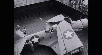 Movie still from “Aircraft Carrier: Guardian of the Seas” (2016), directed by Stephen Low – A black and white photo of men working on an airplane; Wide shot, High angle