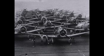 Movie still from “Aircraft Carrier: Guardian of the Seas” (2016), directed by Stephen Low – A group of planes sitting on top of an ocean; Extreme Wide shot, High angle