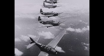 Movie still from “Aircraft Carrier: Guardian of the Seas” (2016), directed by Stephen Low – A black and white photo of a group of fighter jets flying; Extreme Wide shot, Overhead angle