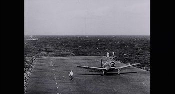 Movie still from “Aircraft Carrier: Guardian of the Seas” (2016), directed by Stephen Low – An airplane on a runway near the ocean; Extreme Wide shot, High angle
