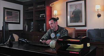 Movie still from “Aircraft Carrier: Guardian of the Seas” (2016), directed by Stephen Low – A man sitting at a desk in front of a computer; Medium shot, Low angle