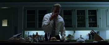 Movie still from “The Game” (1997), directed by David Fincher – A man standing in front of a table eating a sandwich; Medium shot, Low angle