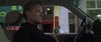 Movie still from “The Game” (1997), directed by David Fincher – A man holding a gun while sitting in the back of a car; Close Up shot, Low angle