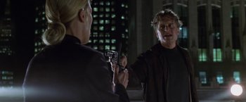 Movie still from “The Game” (1997), directed by David Fincher – A man holding a gun in front of another man in front of a building; Close Up shot, Over the shoulder angle