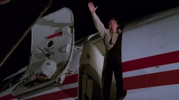 Movie still from “Airplane!” (1980), directed by David Zucker – A man standing on the side of an airplane waving; Wide shot, Overhead angle
