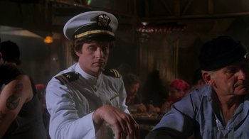Movie still from “Airplane!” (1980), directed by David Zucker – A man in a uniform sitting in front of a group of people; Medium shot, Low angle
