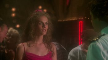 Movie still from “Airplane!” (1980), directed by David Zucker – A woman in a pink dress is standing next to a man in a red shirt; Medium shot, Over the shoulder angle