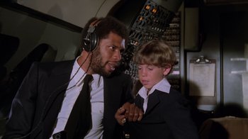 Movie still from “Airplane!” (1980), directed by David Zucker – A man and a young boy wearing headphones and wearing suits; Medium shot, High angle