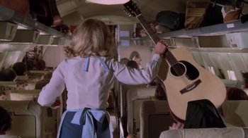 Movie still from “Airplane!” (1980), directed by David Zucker – A woman in a blue apron holding a guitar; Medium shot, High angle