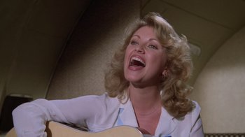 Movie still from “Airplane!” (1980), directed by David Zucker – A woman with curly blonde hair holding a guitar; Close Up shot, Overhead angle